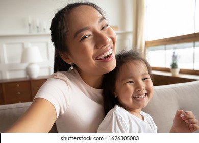 Self-portrait Picture Of Happy Vietnamese Young Mom Or Nanny With Cute Little Biracial Girl Child Pose Together, Selfie Of Overjoyed Asian Mother Have Fun Play With Small Ethnic Daughter At Home