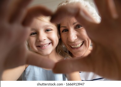Self-portrait picture of smiling mature grandmother and cute little preschooler granddaughter make heart with hands pose look at camera together, happy senior granny and small grandchild take selfie