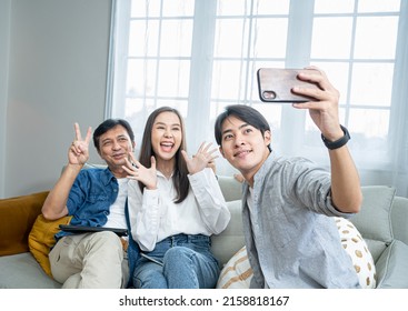 Self-portrait Selfie Of Cheerful Excited Glad Ecstatic Asian Family Taking Photograph With Mobile Phones In The Sofa.The Joy Of Thai Home Living Together.Celebrate In Ester,Christmas Eve,Holiday.