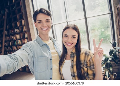 Self-portrait of two attractive cheerful people visiting library showing v-sign at loft industrial interior indoors open space