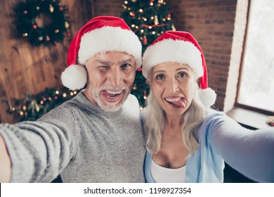 Self-portrait of two beautiful charming cheerful glad positive grey-haired people married spouses granddad grandma showing tongue out winking blinking near eve noel fir tree - Powered by Shutterstock