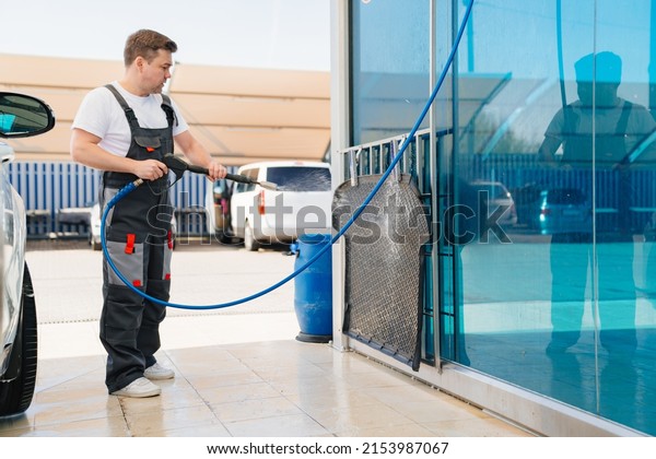 self-service car wash. a man in a work jumpsuit\
washes the car mat from a hose. professional cleaning of transport.\
car washer.