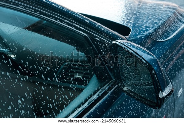Self-service car wash station. Active foam is\
cleaning a dirty sedan car. Details of the foam on car window and\
body parts.
