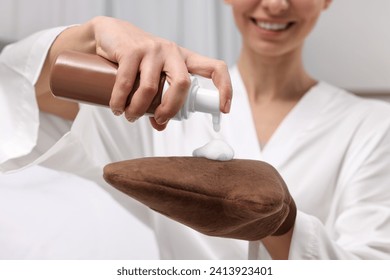 Self-tanning. Woman applying cosmetic product onto tanning mitt indoors, closeup