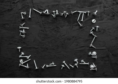 Self-tapping screws and screws of various sizes are randomly arranged on a black wooden background. Screws and screws as background. Place for your text.
