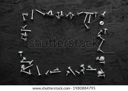 Self-tapping screws and screws of various sizes are randomly arranged on a black wooden background. Screws and screws as background. Place for your text.