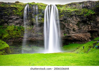 Seljalandsfoss, Iceland waterfall with long exposure of white water cliff in green summer rocky landscape and people walking on trail