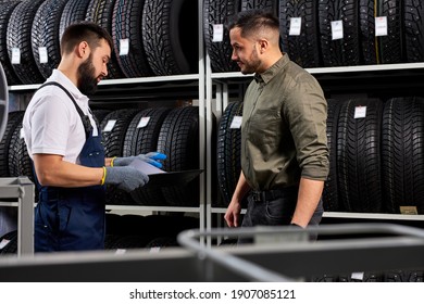 seller auto mechanic helping man to choose tires in car store, showing and giving information about the best one