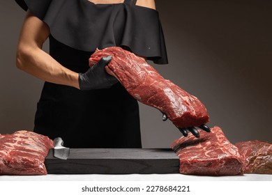 Seller in black uniform in shop market holds big piece of fresh raw calf beef bull sirloin ribeye steak . seller shows costumer meat. closeup front view. banners advertising advertisment banner mockup - Powered by Shutterstock