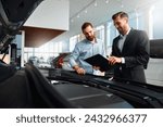 Seller or car salesman and client or customer in car dealership presenting the engine performance of new and used cars in the showroom, the men looking under the hood