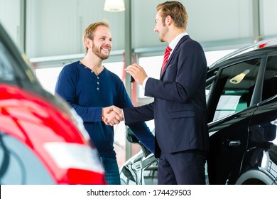 Seller or car salesman and customer in auto dealership, they shaking hands, hands over the car keys and seal the purchase of the auto or new car