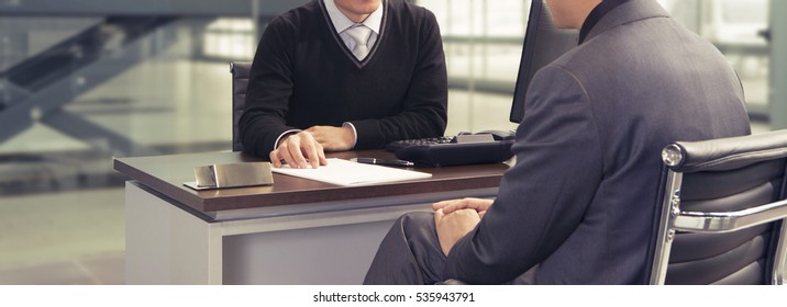 Seller or car salesman and customer in auto dealership, they discussing on the documents inside the office