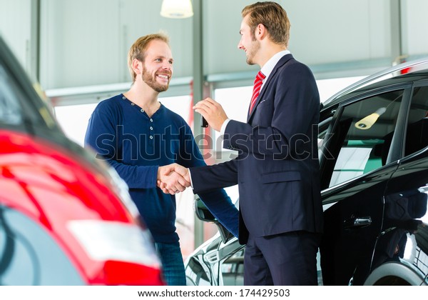 Seller or car salesman and customer in auto\
dealership, they shaking hands, hands over the car keys and seal\
the purchase of the auto or new\
car