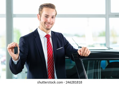 Seller Or Car Salesman In Car Dealership With Key Presenting His New And Used Cars In The Showroom