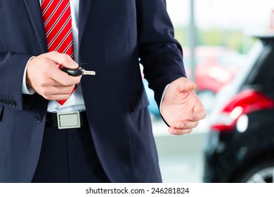 Seller Or Car Salesman In Car Dealership With Key Presenting His New And Used Cars In The Showroom