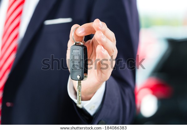 Seller or car salesman in car\
dealership with key presenting his new and used cars in the\
showroom