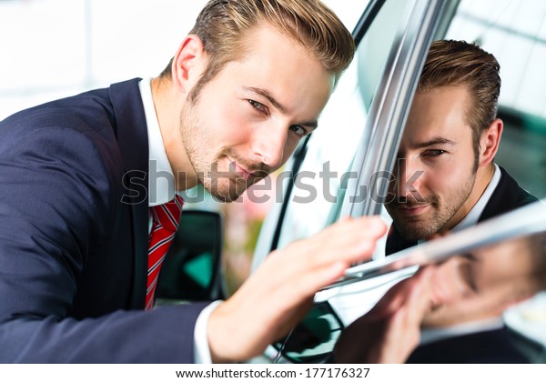 Seller or\
car salesman in car dealership presenting the reflecting car paint\
of his new and used cars in the\
showroom