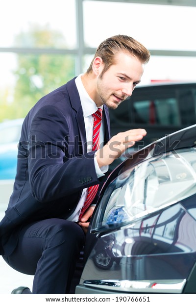 Seller or\
car salesman in car dealership presenting the reflecting car paint\
of his new and used cars in the\
showroom