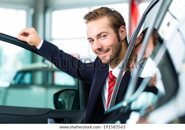 Seller or car salesman in car dealership\
presenting his new and used cars in the\
showroom