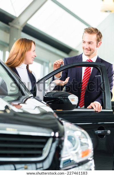 Seller or car\
salesman and female client or customer in car dealership presenting\
the interior decoration of new and used cars in the showroom and\
hands over the car keys