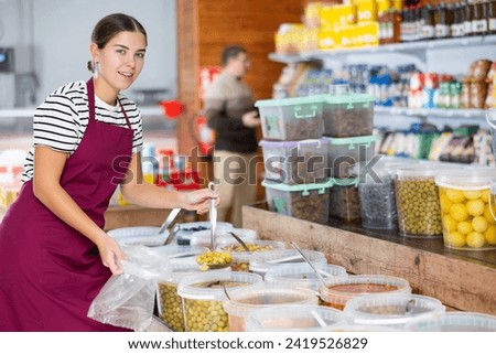 Seller girl in supermarket scooping marinated green olives