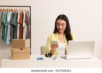 Seller with laptop and parcels using smartphone in office. Online store