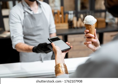 Seller in makes contactless payment for a client in the ice cream shop, close-up - Powered by Shutterstock