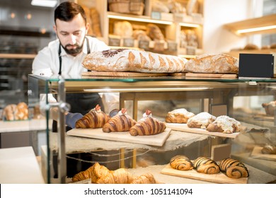 Seller putting delicious croissants on the store showcase of the bakery house