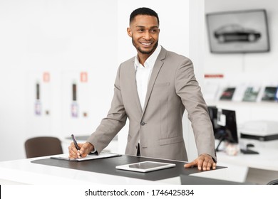 Selling Cars. Auto Dealer Man Standing At Counter Working In Automobile Dealership Office.