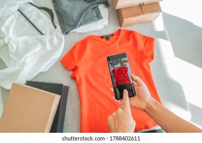 Selling online by taking photo of clothes with phone app and doing e-commerce business woman at home with shipping boxes.
