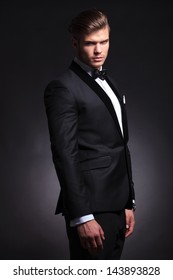 Semi Profile Picture Of An Elegant Young Fashion Man In Tuxedo Looking At The Camera And Frowning. On Black Background