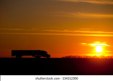 Semi tractor trailer silhouetted with setting sun.
