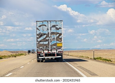 Semi Tractor Trailer Truck On Desert Highway With Shiny Back Reflecting Sky And Pavement In Blurry Pattern - More Trucks And Mountain Range In Distance