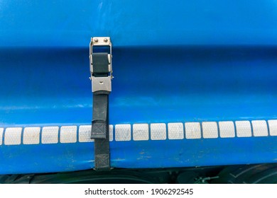 Semi Truck Blue Curtain Side Trailer Ratchet Strap Close Up With Safety Reflective Squares Strip And With Copy Space.