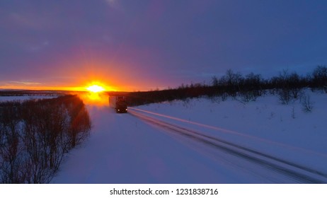 Semi truck driving on snow covered highway trough forest landscape at sunset