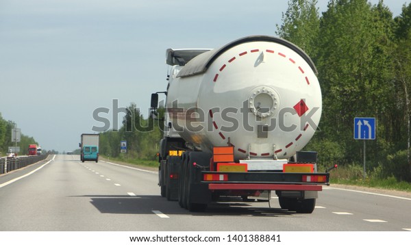 Semi truck with\
propane tank moving on asphalt road on a summer day - ADR dangerous\
cargo, side rear view