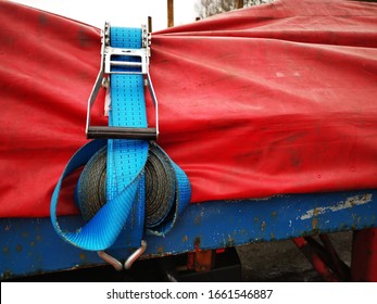 Semi Truck Trailer Carrying Steel Covered With A Red Tarp And Secured With Ratchet Straps. Close Up Of The Strap Rolled Up And Held In Place. 