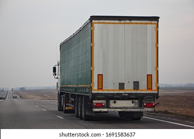 Semi truck van drive on dry suburban asphalt highway at spring day, rear-side view – international logistics, cargo transportation, trucking industry