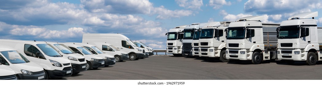 Semi trucks and delivery vans are parked in rows. Commercial fleet