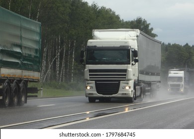 Semi trucks lorry convoy move on suburban wet asphalted highway front view on cloudy summer day, safety drive overtake on rain slippery road on green forest background