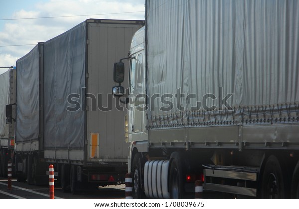 A lot semi trucks traffic jam queue on warehouse\
at summer day side view, international cargo delivery traffic\
problem, illustration concept
