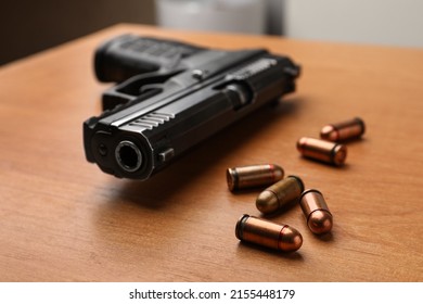 Semi-automatic pistol and bullets on wooden table indoors, closeup