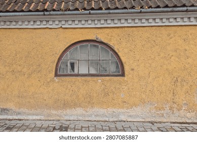 Semi-circular arched window set into a weathered yellow wall, Estonia, Europe.