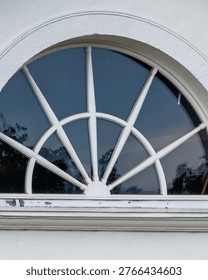 Semicircular fanlight window featuring a sunburst design on a white building exterior