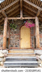 Semicircular Wooden Door In The Back Made Of Stones And A Wooden Porch With Steps And A Suspended Flowerpot