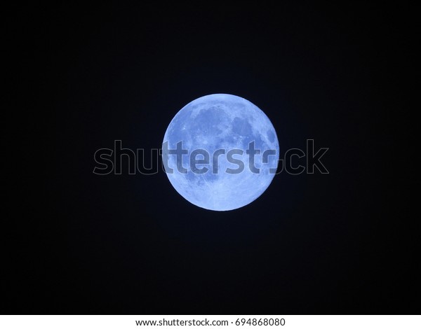 Semi-close up view of a beautiful blue moon in the\
night sky.