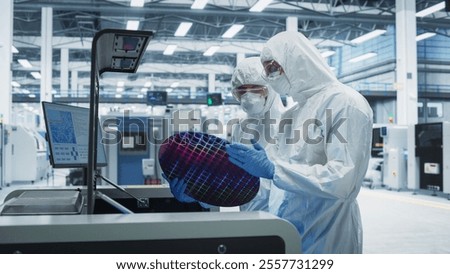 Semiconductor Production At Electronics Manufacturing Facility: Two Specialists In Sterile Suits Taking Out Silicon Wafer From Soldering Jet Printer And Inspecting. Engineers Making Computer Hardware