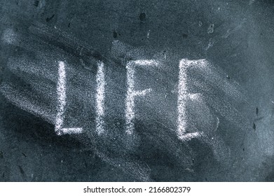 The Semi-erased Word LIFE On The Black Chalkboard. Handwritten Word. Fuzzy Letters On Black Surface.