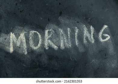 The Semi-erased Word MORNING On The Black Chalkboard. Handwritten Word. Fuzzy Letters On Black Surface. The Concept Of Changing The Time Of Day