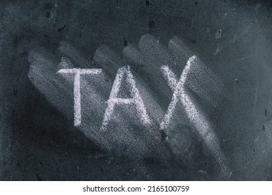 Semi-erased Word TAX On Black Chalkboard. Handwritten Word. Fuzzy Letters On Black Surface.